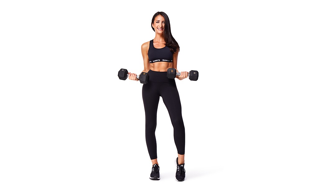 Barry’s instructor wearing a black top standing confidently smiling against a white background holding weights out to the side