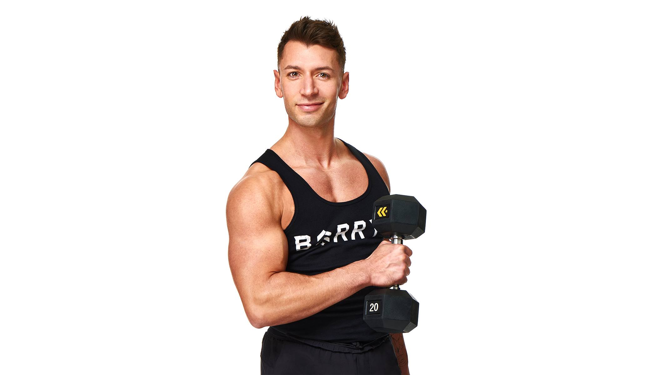Barry’s instructor wearing a black top standing confidently smiling against a white background holding a weight