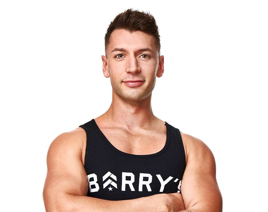 Barry’s instructor wearing a black top standing confidently smiling against a white background