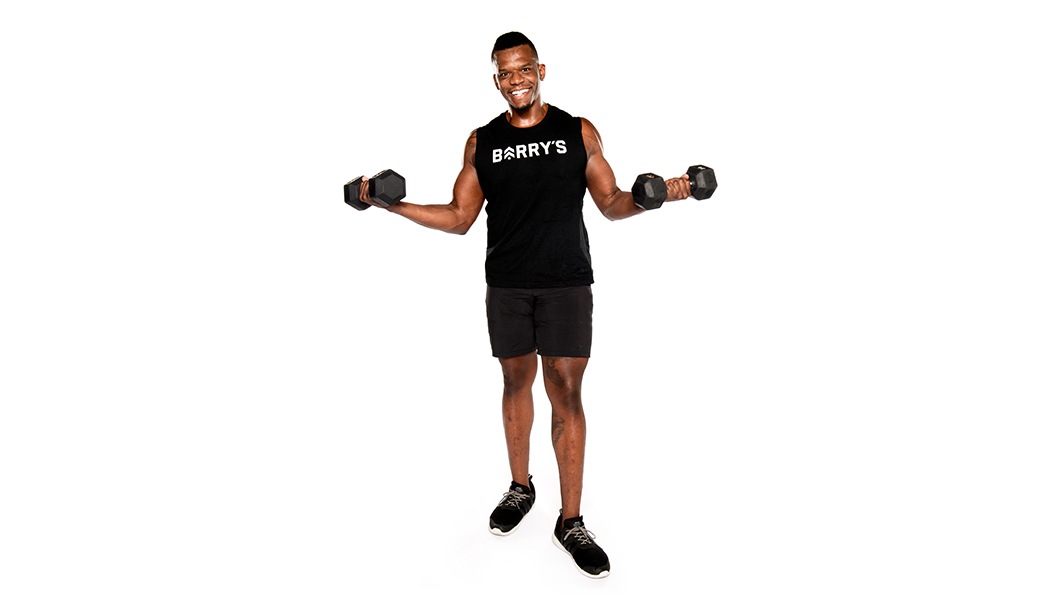 Barry's instructor standing confidently with weights, wearing a black tank top against a white background, ready for the next workout challenge.