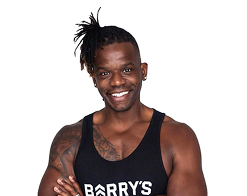 Barry's instructor standing confidently with arms crossed in front, wearing a black tank top against a white background, ready for the next workout challenge.