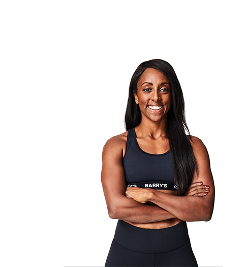 El instructor de Barry, con una camiseta negra, está de pie, sonriendo con confianza sobre un fondo blanco.