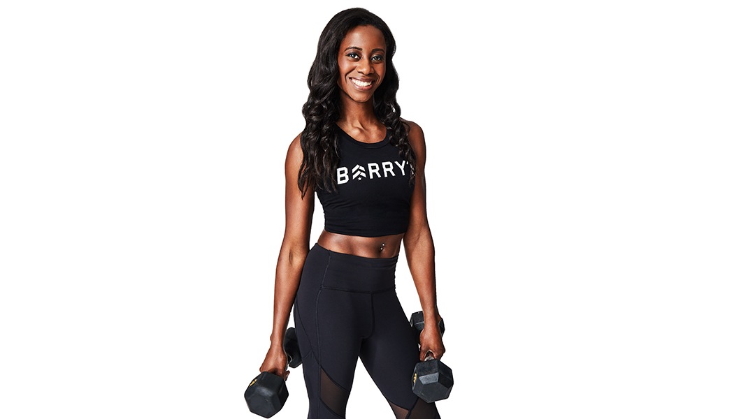 Barrys instruktör i svart topp står självsäkert och ler mot en vit bakgrund och håller vikter