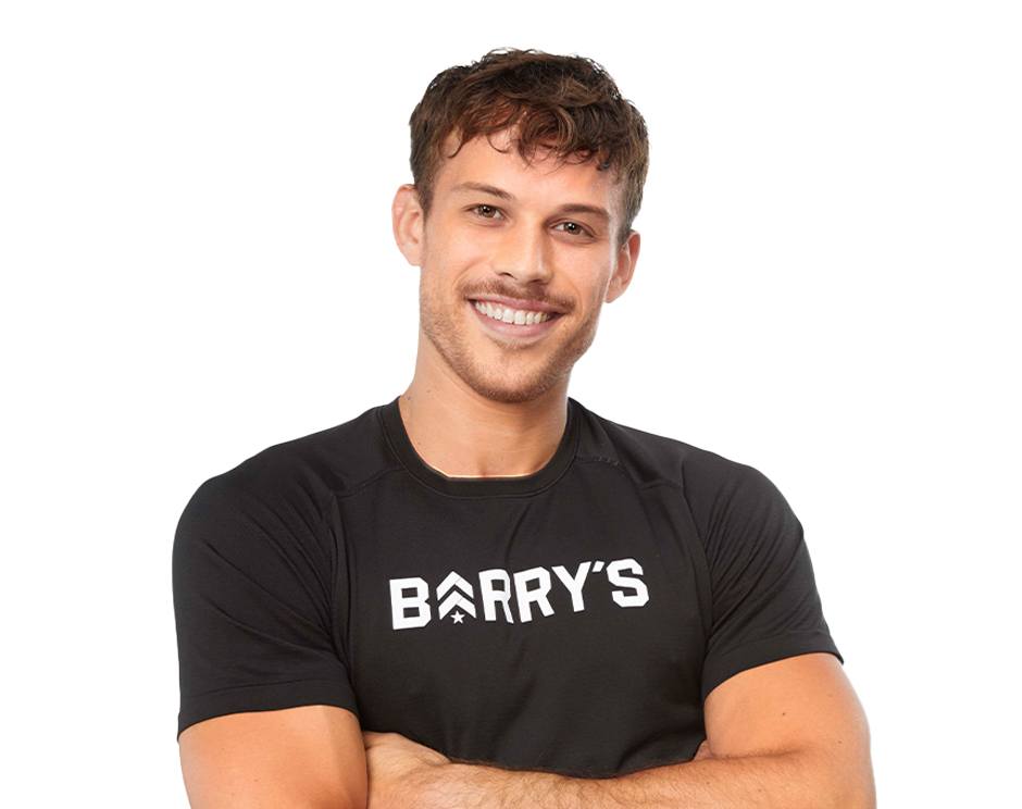 Barry's instructor standing confidently with arms crossed, wearing a black top against a white background, ready for the next workout challenge.