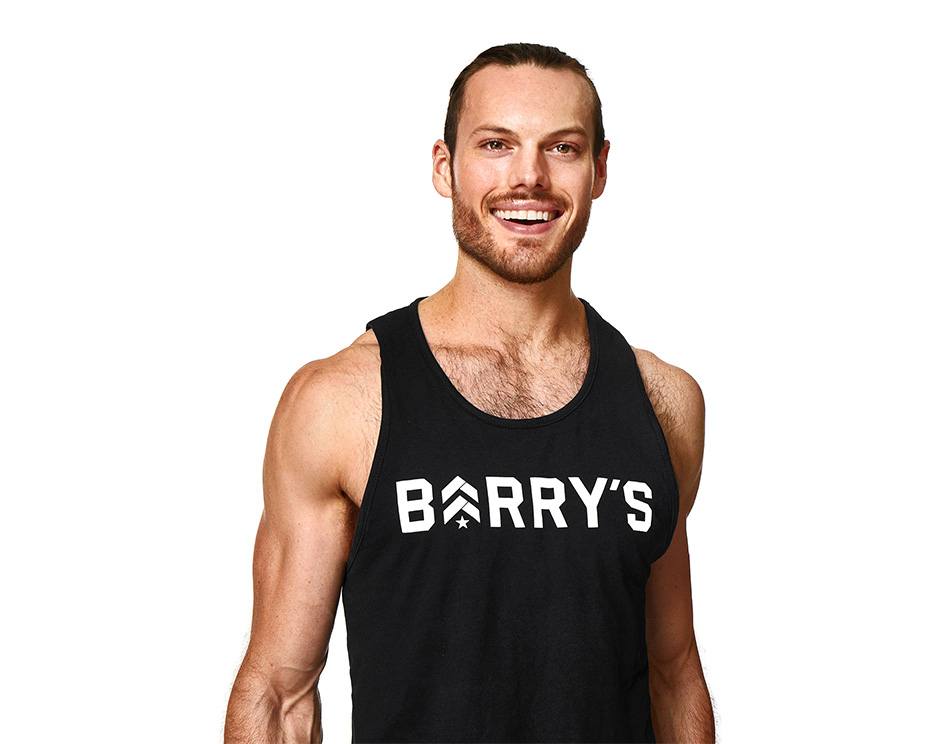 Barry’s instructor wearing a black top standing confidently smiling against a white background