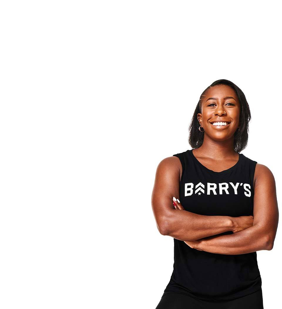 Barry’s instructor wearing a black top standing confidently smiling against a white background