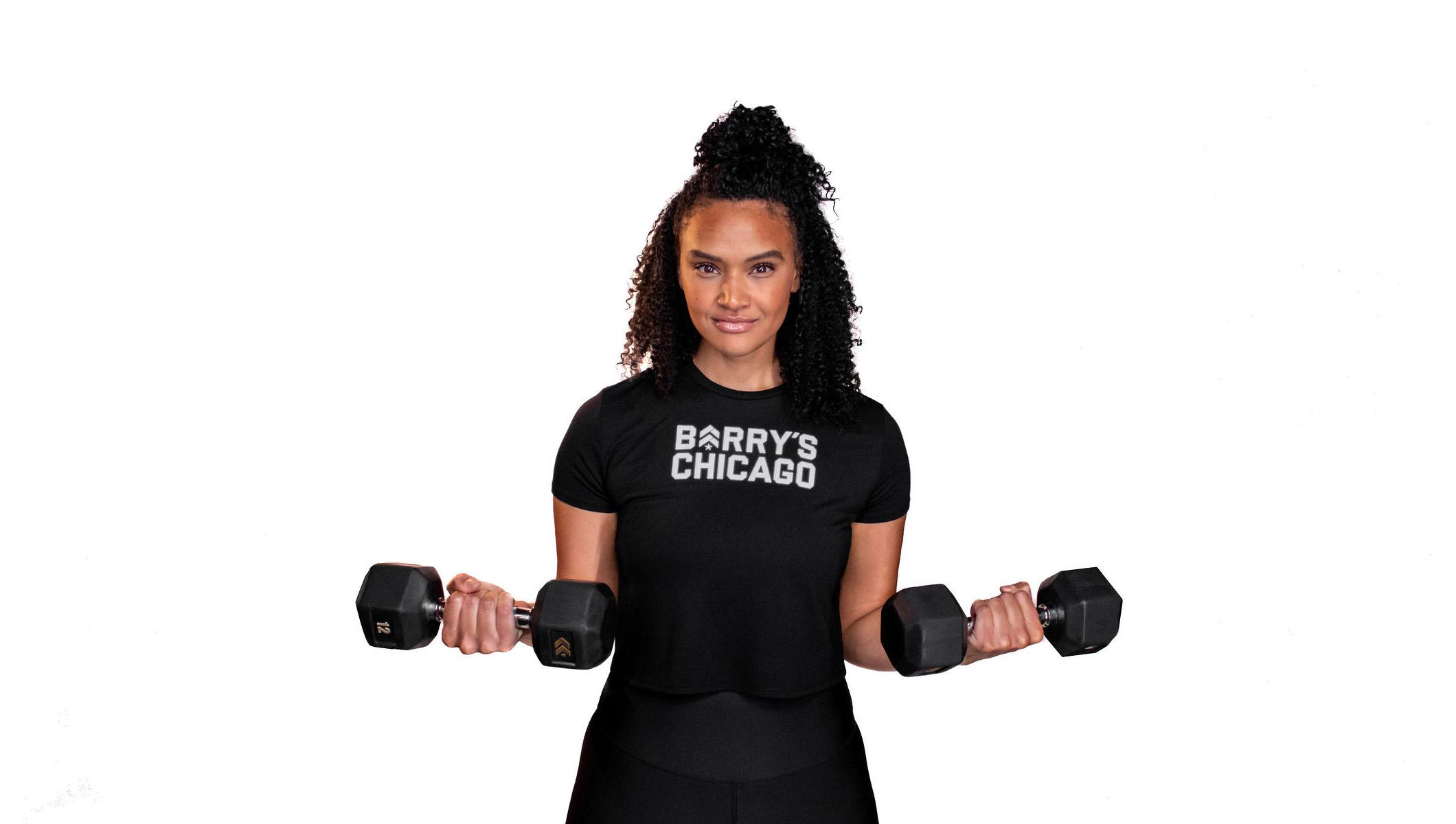 Barry's instructor standing confidently holding weights wearing a black top against a white background.