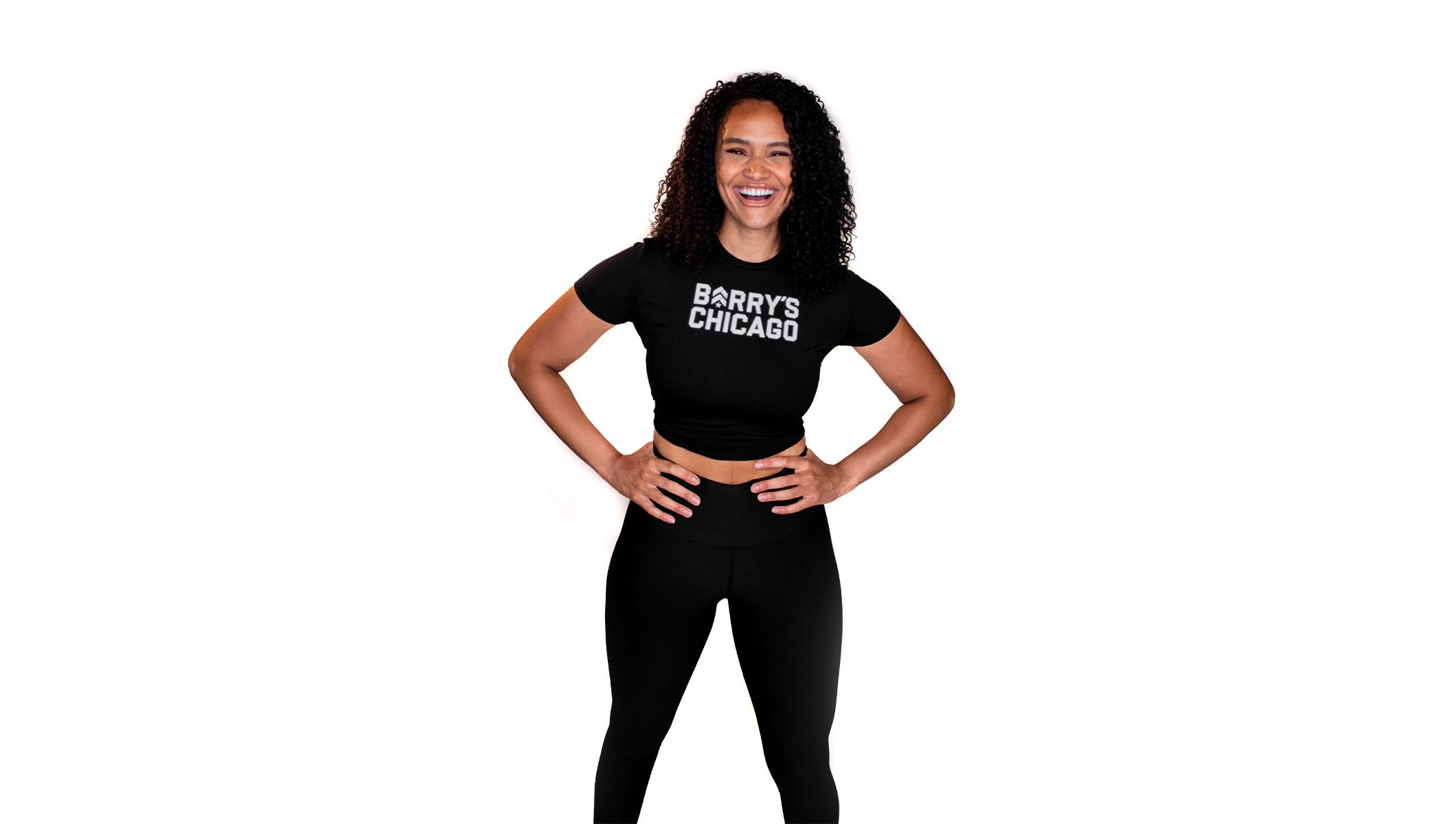 Barry's instructor standing confidently with hands on hips wearing a black top against a white background.