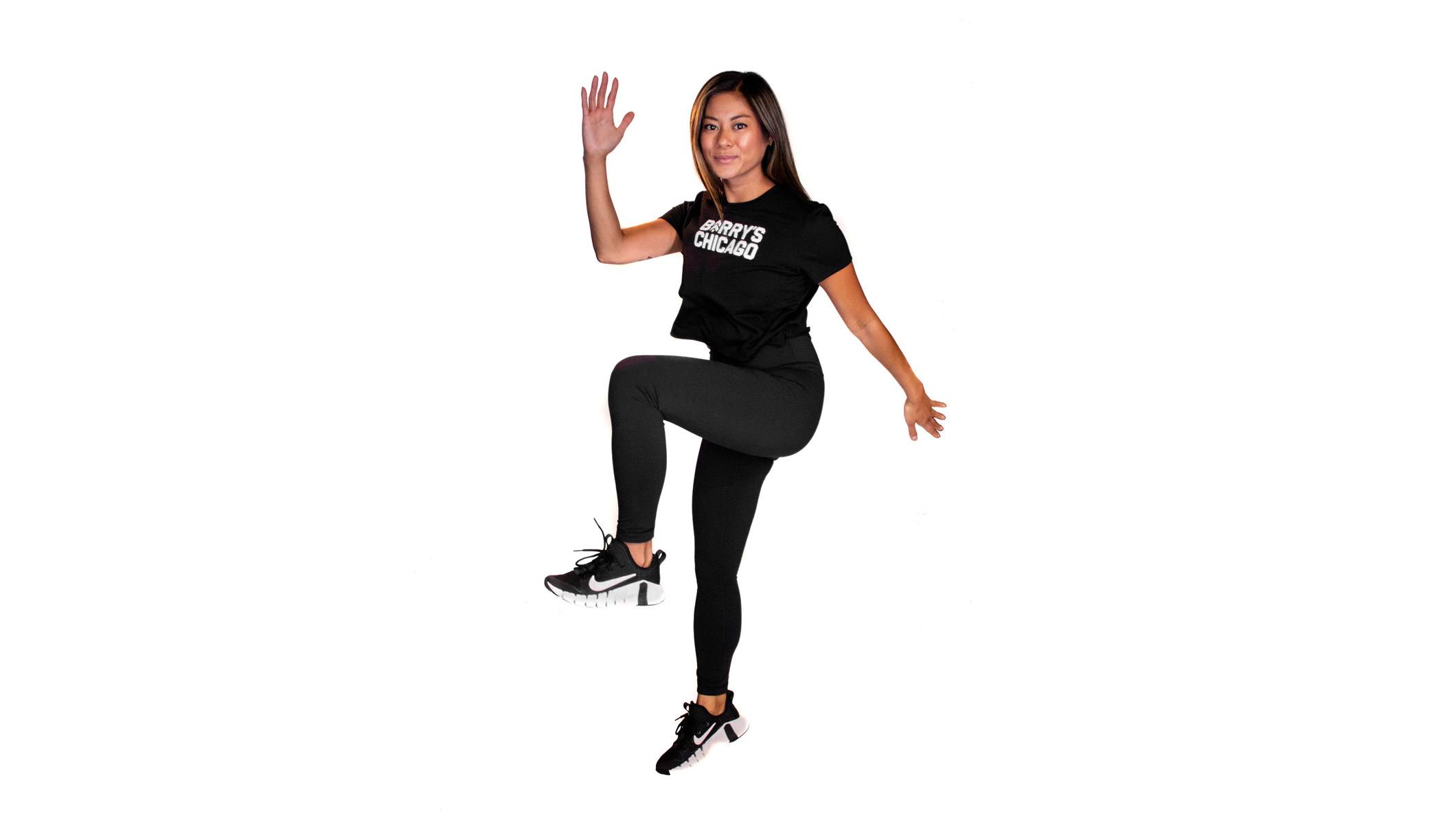 Barry's instructor in a running jump confidently wearing a black top against a white background.