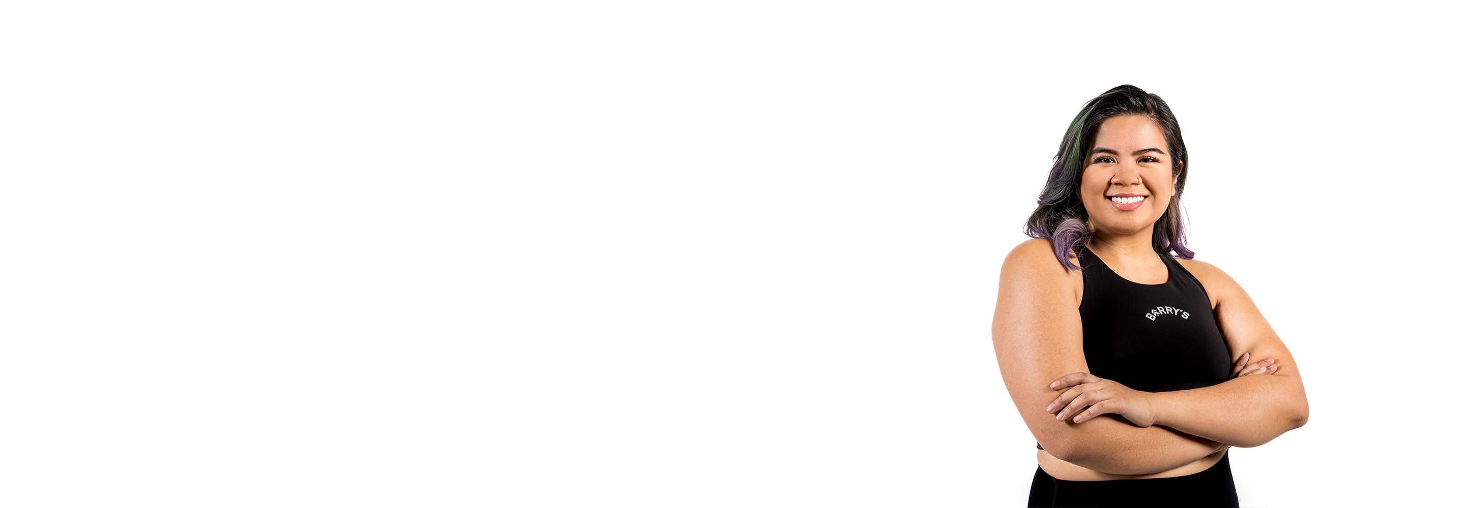 El instructor de Barry, con una camiseta negra, está de pie, sonriendo con confianza sobre un fondo blanco.