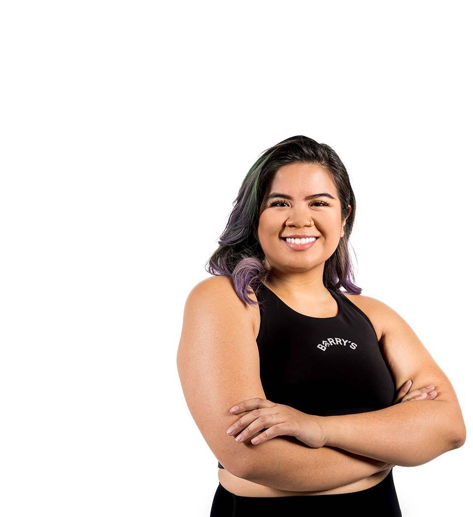 El instructor de Barry, con una camiseta negra, está de pie, sonriendo con confianza sobre un fondo blanco.