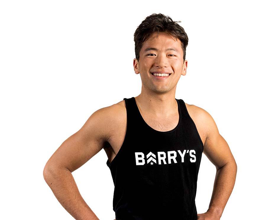 Barry’s instructor wearing a black top standing confidently smiling against a white background