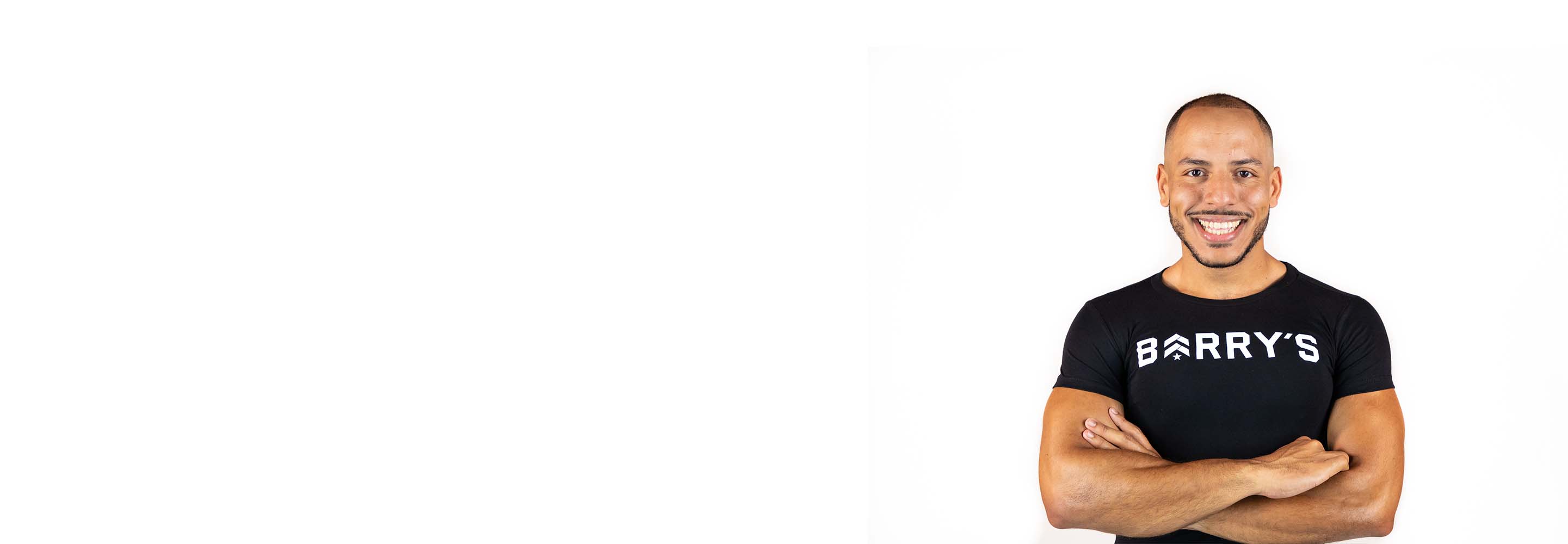 Barry's instructor standing confidently with arms crossed in front, wearing a black tank top against a white background, ready for the next workout challenge.