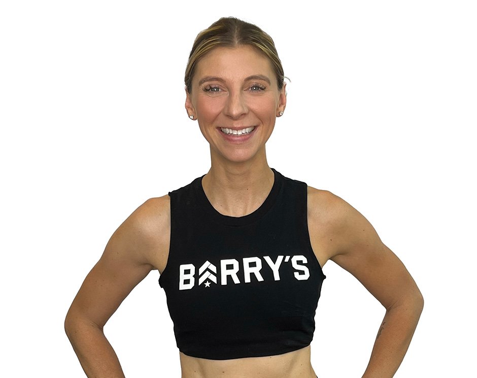 Barry’s instructor wearing a black top standing confidently smiling against a white background