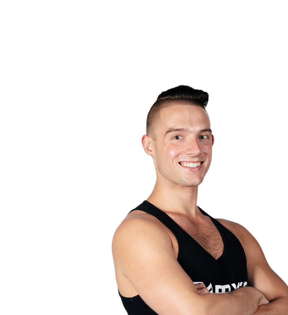 El instructor de Barry aparece de pie, con confianza, vistiendo una camiseta negra sobre un fondo blanco.