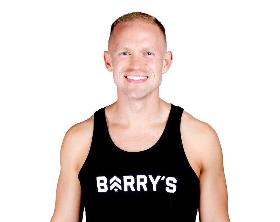 Barry’s instructor wearing a black top standing confidently smiling against a white background