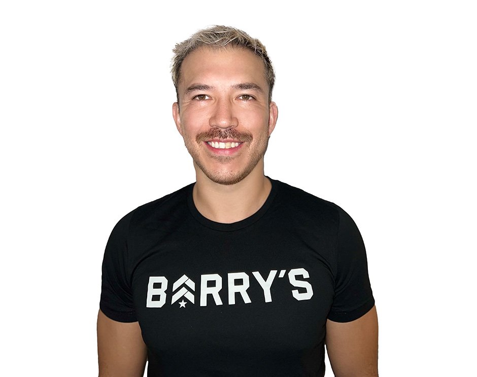 Barry’s instructor wearing a black top standing confidently smiling against a white background