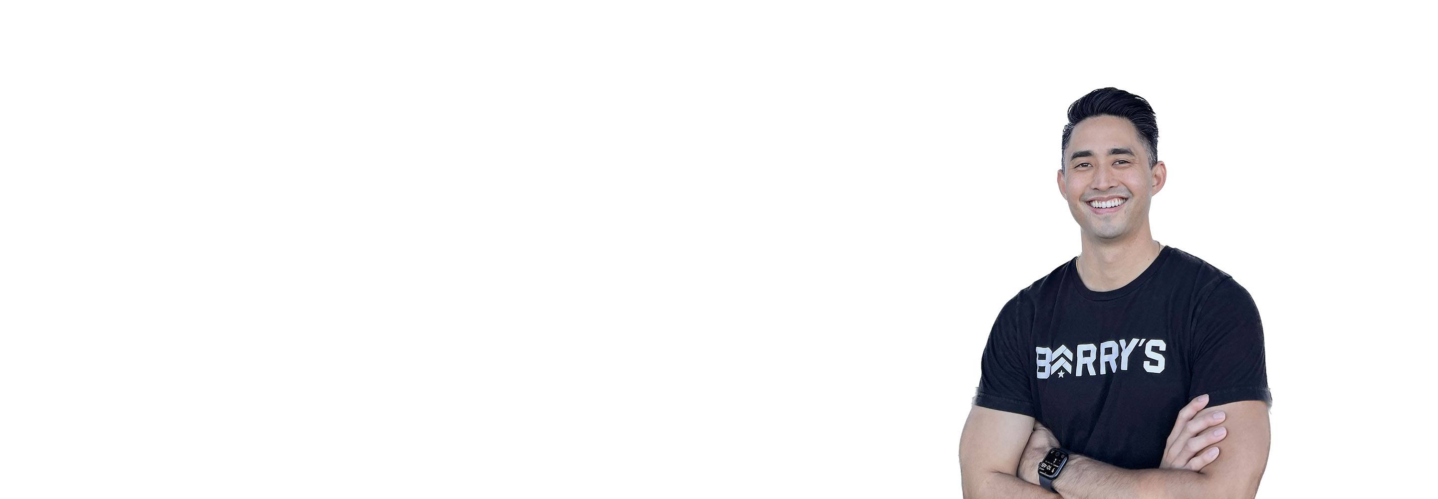 Barry's instructor standing confidently with arms crossed in front, wearing a black tank top against a white background, ready for the next workout challenge.