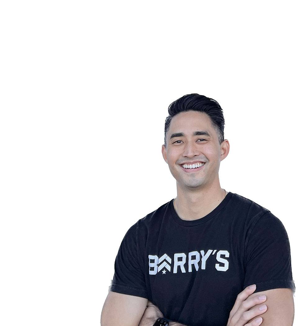 Barry's instructor standing confidently with arms crossed in front, wearing a black tank top against a white background, ready for the next workout challenge.