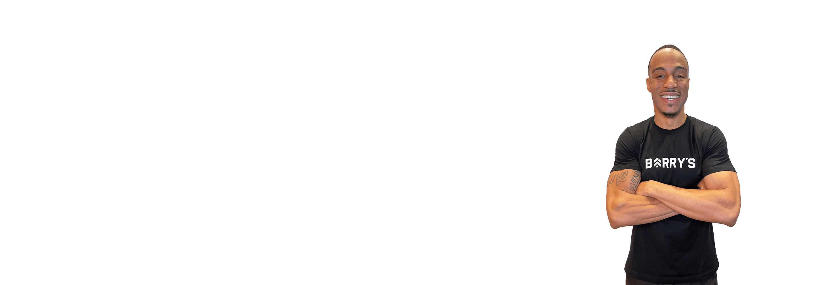 Barrys instruktör står självsäkert med armarna i kors iförd en svart topp mot en vit bakgrund.