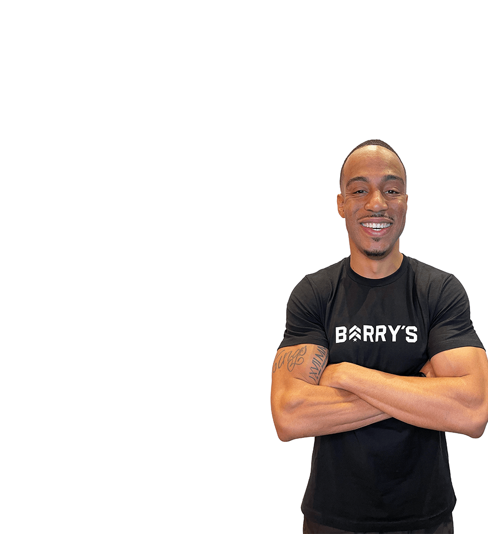 Barrys instruktör står självsäkert med armarna i kors iförd en svart topp mot en vit bakgrund.