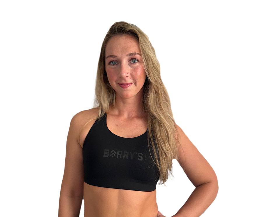 Barry’s instructor wearing a black top standing confidently smiling against a white background