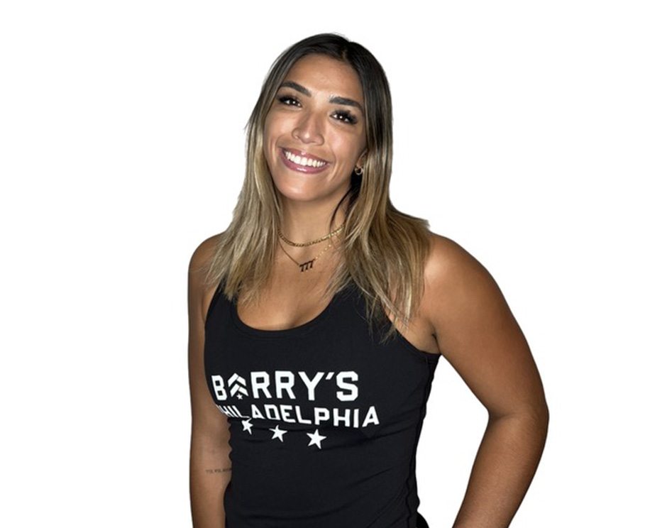 Barry’s instructor wearing a black top standing confidently smiling against a white background
