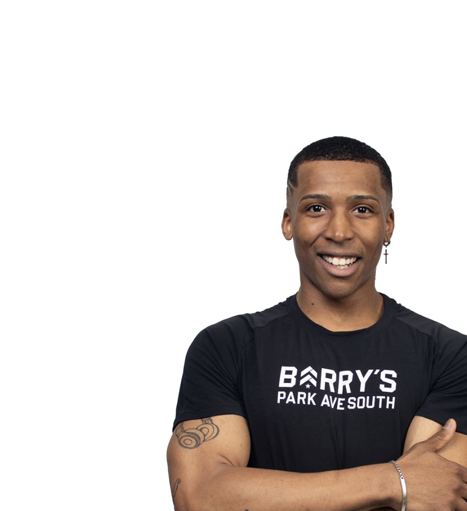 Barry’s instructor wearing a black top standing confidently smiling against a white background