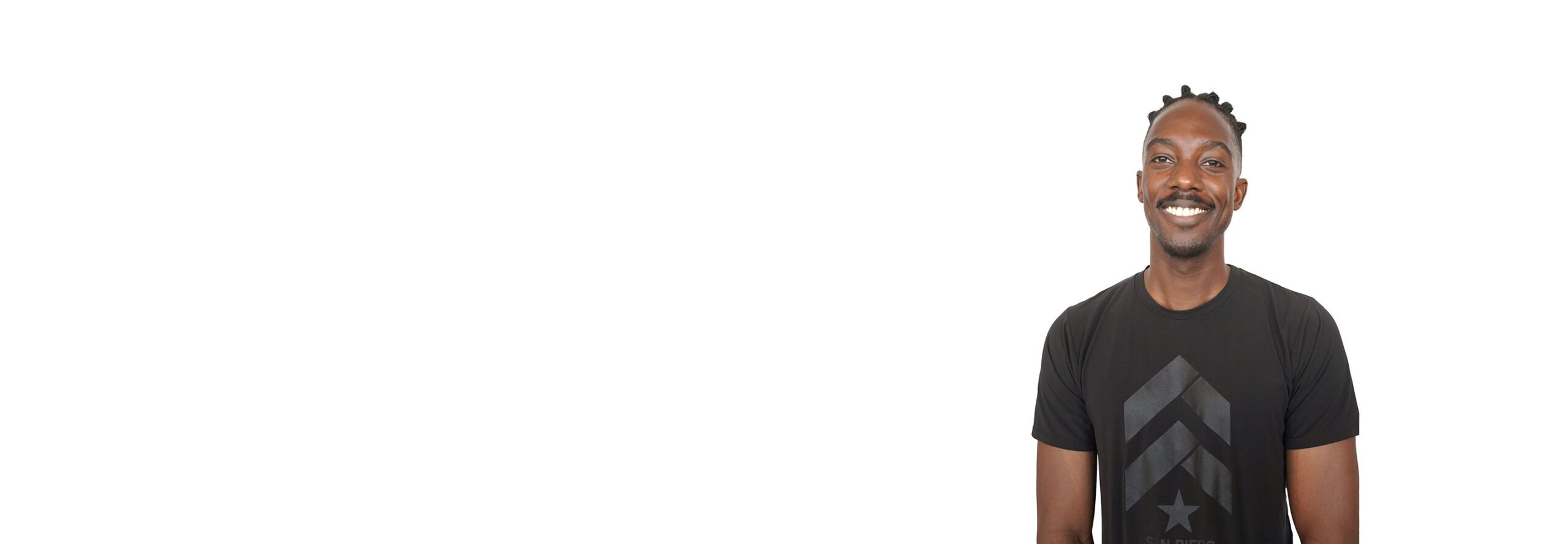 El instructor de Barry se mantiene firme, vistiendo una camiseta sin mangas negra sobre un fondo blanco, listo para el próximo desafío de entrenamiento.