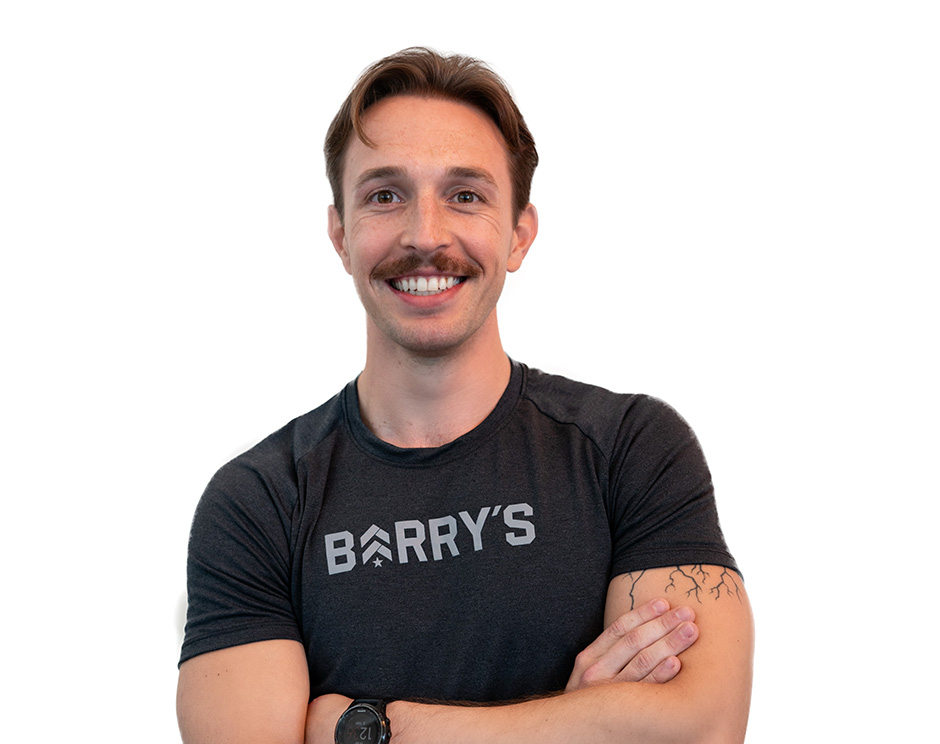 Barry’s instructor wearing a black top standing confidently smiling against a white background