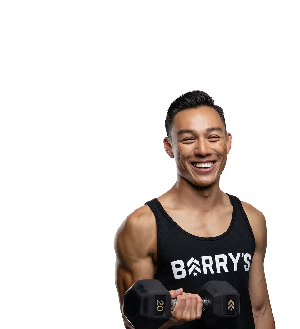 Barry’s instructor wearing a black top standing confidently smiling against a white background.